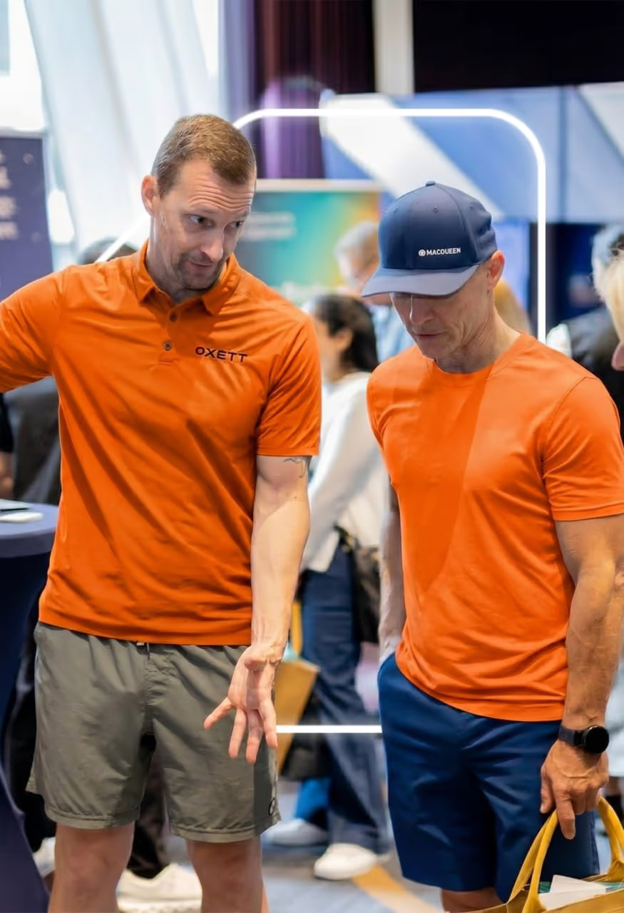 Dos miembros del equipo de SimYak con camisetas naranjas de la marca conversando en una feria de tecnología de viajes