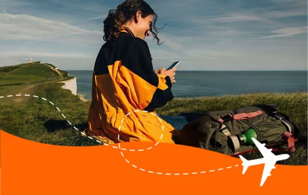 Traveller using her phone on a grassy coastal clifftop above the sea while connected with a SimYak eSIM